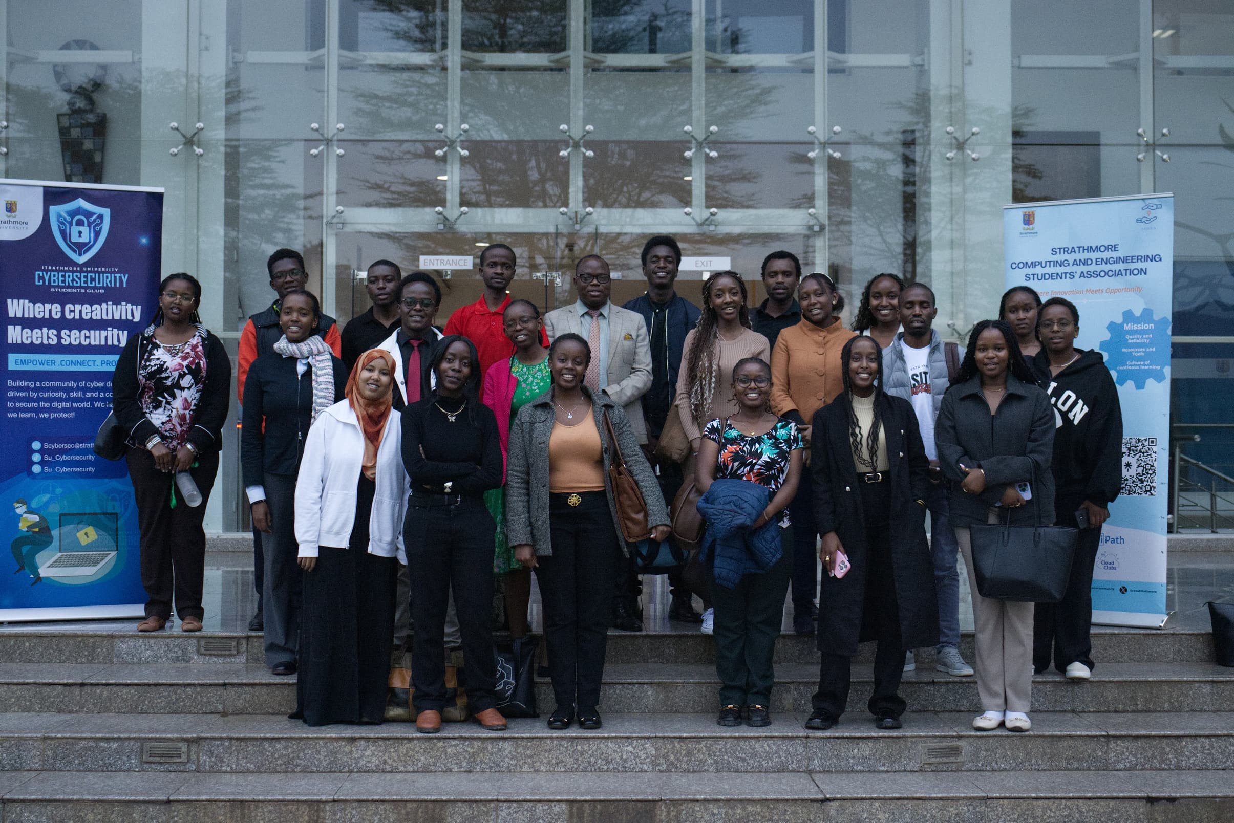 SCESA members and guests on the steps outside a Strathmore University building, between a Cybersecurity Club banner and a SCESA banner